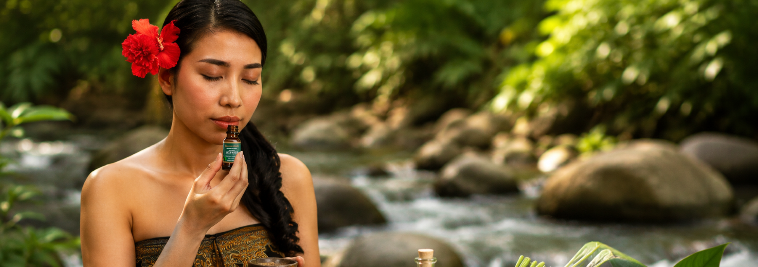 Woman enjoying a Biossentials essential oil aromatherapy ritual beside a tropical stream